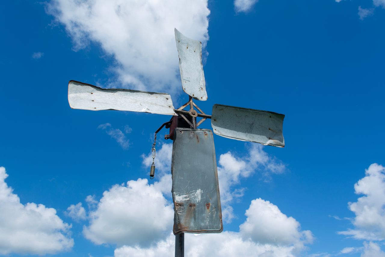 A rustic metal windmill stands tall under a vivid blue sky with scattered clouds.