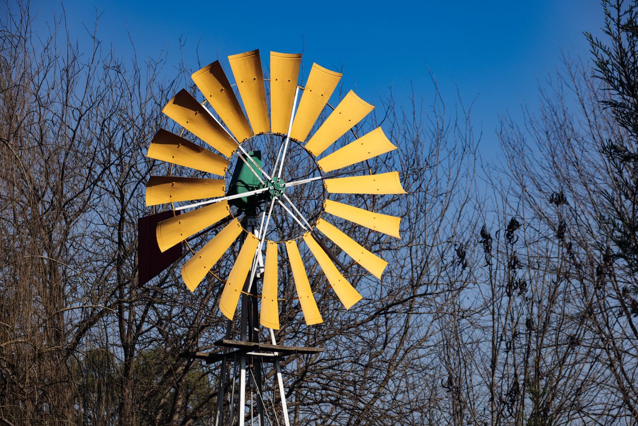 A yellow windmill stands tall against a clear blue sky with bare winter trees in background.